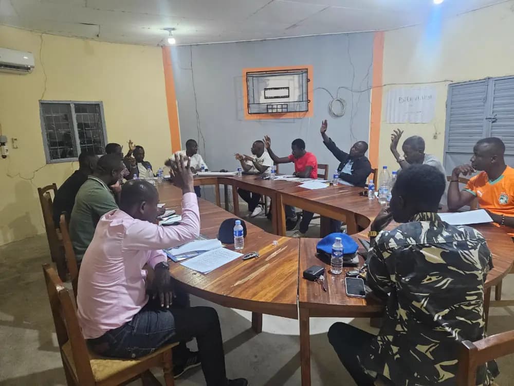 Une dizaine de militants assis autour de tables disposées en U lèvent la main lors d’un vote, dans une salle de réunion.